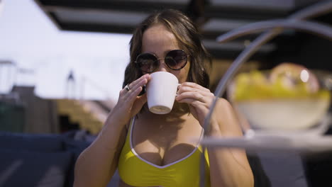 slow motion shot of a happy attractive female in a bikini taking a hot drink