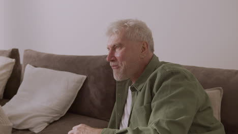 happy elderly man eating caramel popcorn and watching game on tv while lying on sofa at home