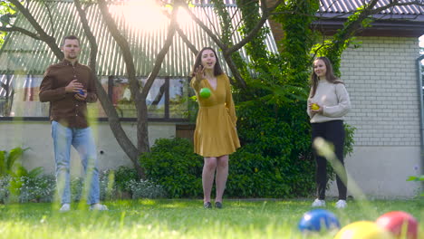 front view of caucasian young woman throwing a green petanque ball in the park on a sunny day while her friends wait their turns