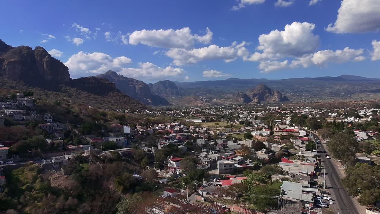 Backward aerial view of Oaxtepec and Tlayacapan, Morelos, surrounded by rocky mountains under a cloudy blue sky
