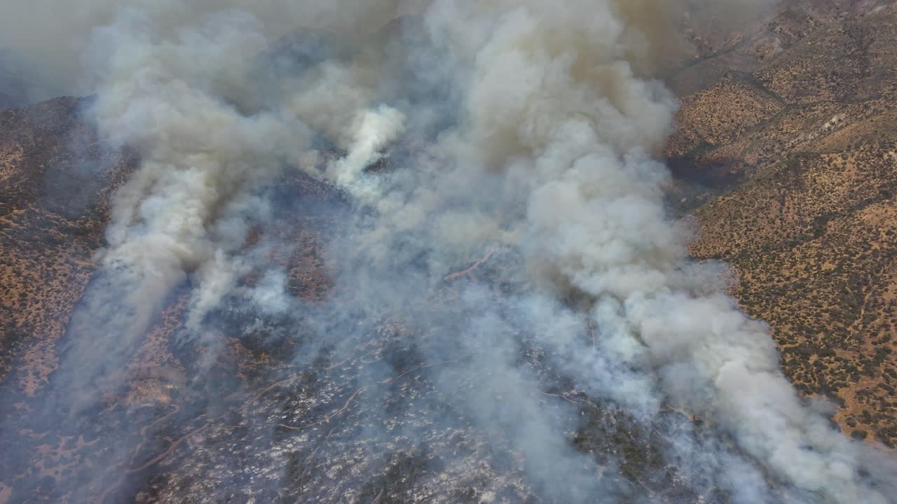 Ripresa aerea dall'alto con drone ad angolazione elevata che guarda direttamente verso il basso, nel denso fumo di un incendio che oscura la terra bruciata e la vegetazione sottostante in Cile e in 4K