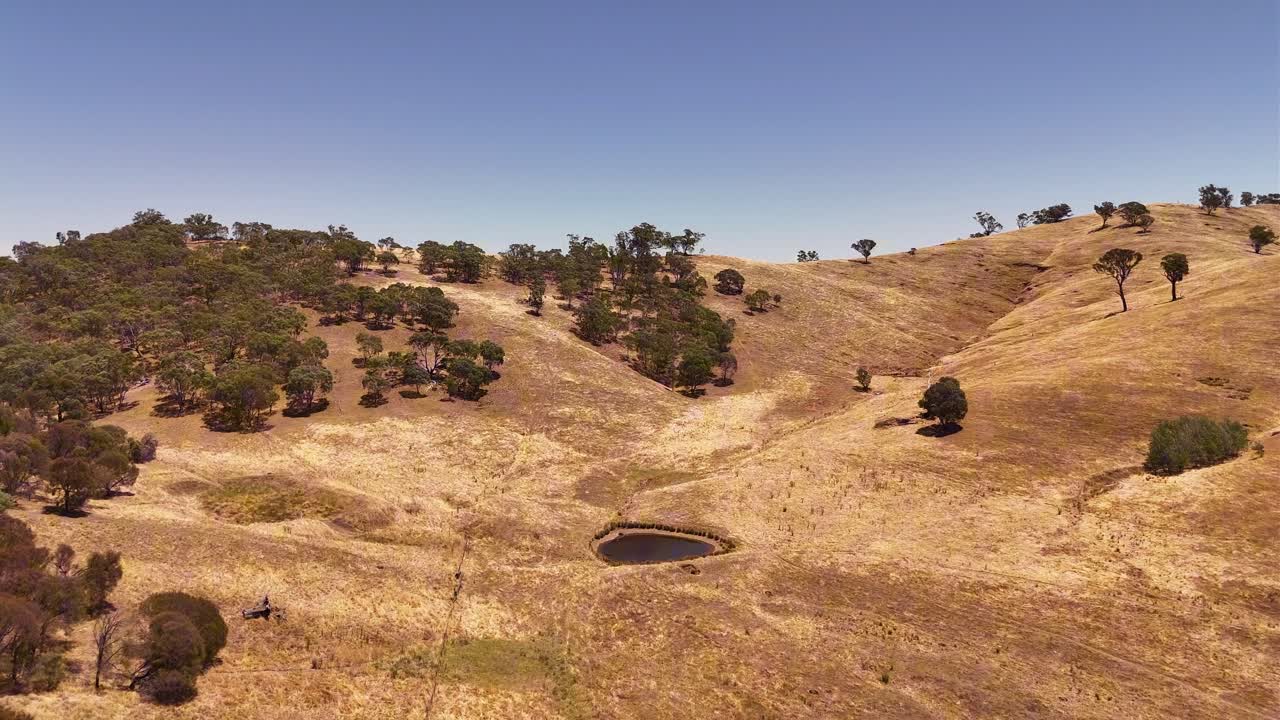 Wagga Hill, terreno ondulato e arido disseminato di alberi radi e terra polverosa sotto un cielo luminoso, bacino di contenimento al centro