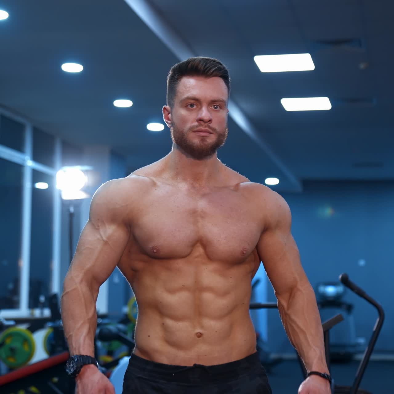 Half length portrait of shirtless sportsman. Muscular bodybuilder with naked torso in the gym. Handsome man with perfect athletic body moving to camera.