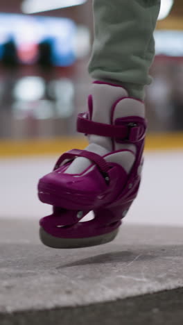 vista de cerca de una persona con patines de hielo púrpura entrando en la pista de hielo, el fondo está borroso, destacando las luces y el entorno dinámico de la pista de patinaje