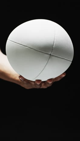 vertical video of hand of african american man holding white rugby ball on black background