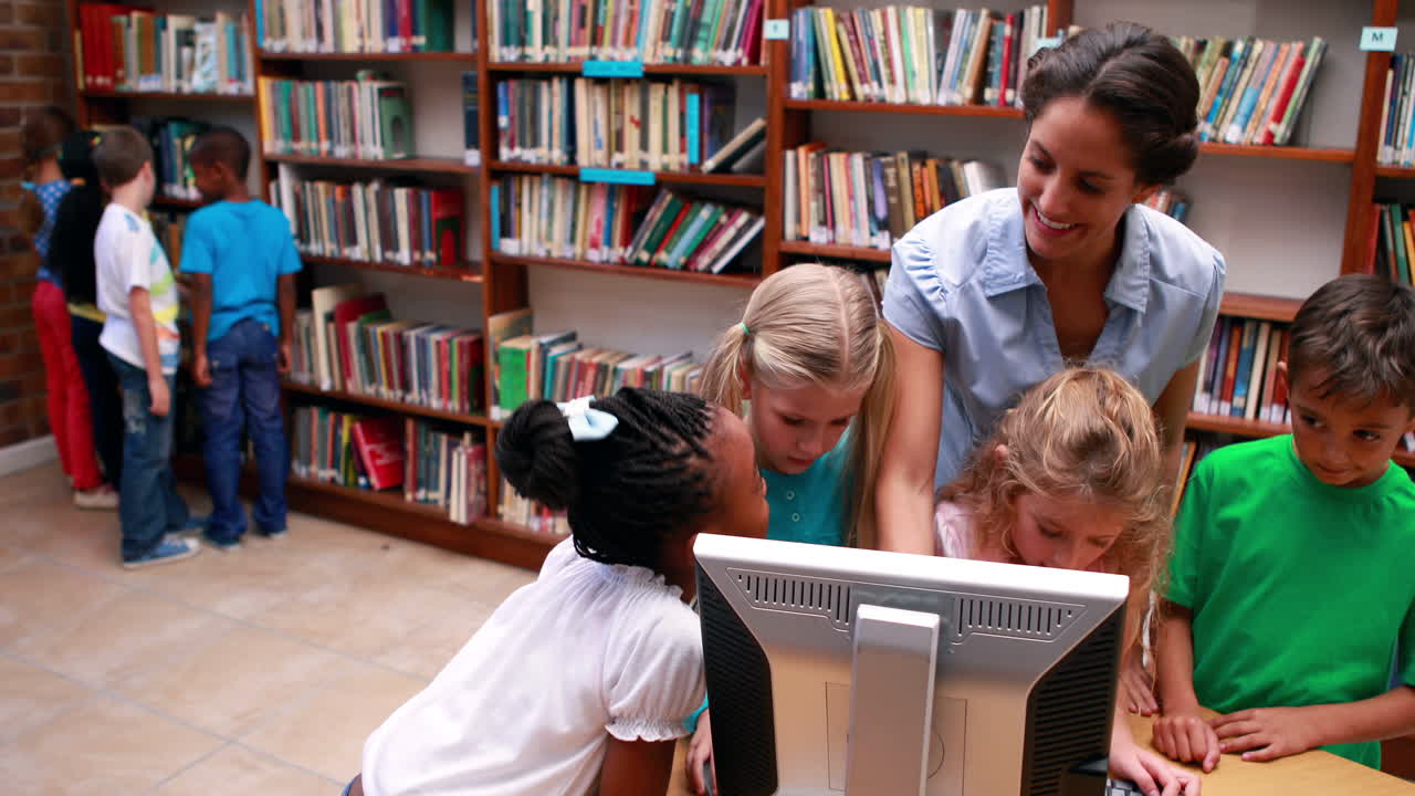 alumnos mirando la computadora en la biblioteca con su maestro
