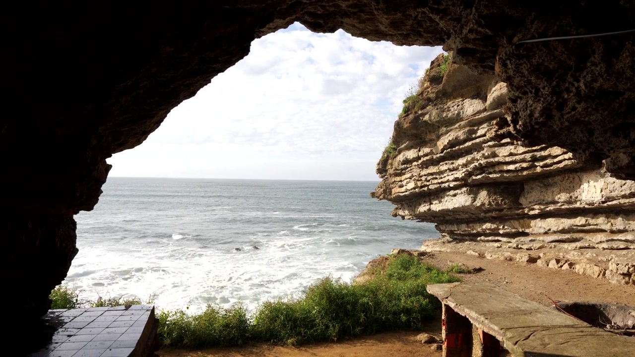 View of the Cantabrian Sea from inside Cucabrera Cave with waves crashing against cliffs on a cloudy day