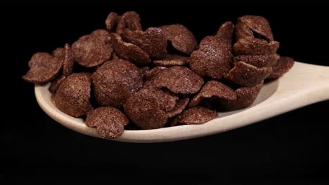 chocolate cereal flakes tumble from a wooden spoon against a black background, highlighting texture and motion