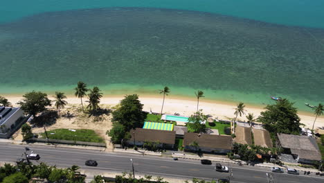 Road-and-small-homes-of-tropical-island-coastline-in-Thailand,-aerial-view