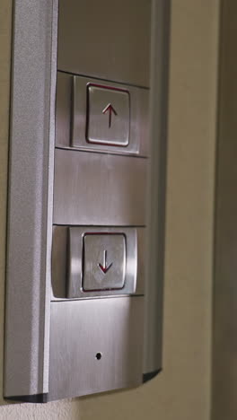 Close-up of hand pressing elevator button, modern metallic elevator panel, upward direction symbol, professional environment, business building, corporate setting, modern design