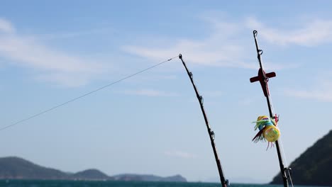 a fishing rod gently sways on a boat against a clear blue sky and distant hills in phuket, thailand