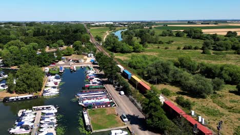 Vista-Aérea-De-Un-Largo-Tren-De-Mercancías-Que-Pasa-Por-Un-Puerto-Deportivo-En-Ely,-Cambridgeshire,-Reino-Unido