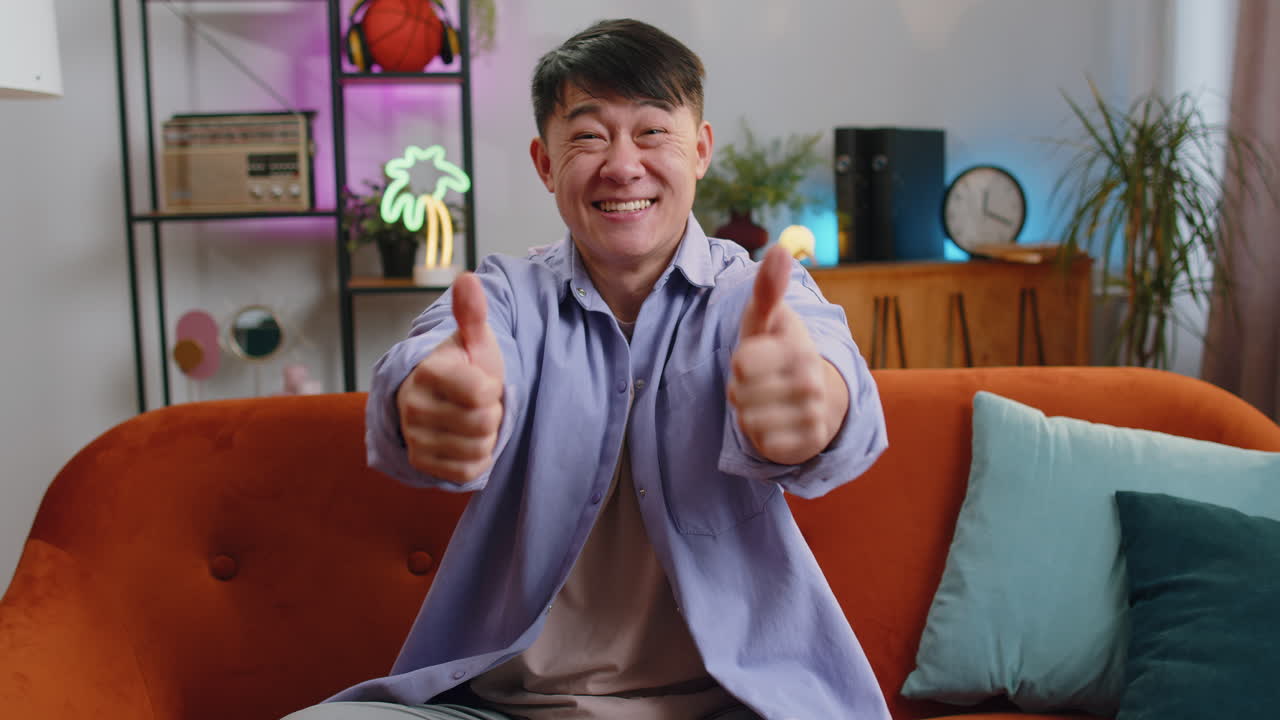 Happy asian man looking approvingly at camera showing thumbs up like positive sign good news