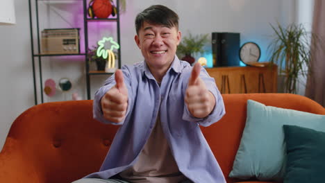 happy asian man looking approvingly at camera showing thumbs up like positive sign good news