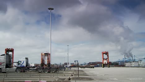 amplia fotografía de un ocupado puerto industrial con camiones y grúas bajo un cielo nublado