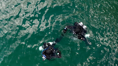 top down aerial view of two scuba divers immersing into lake waters