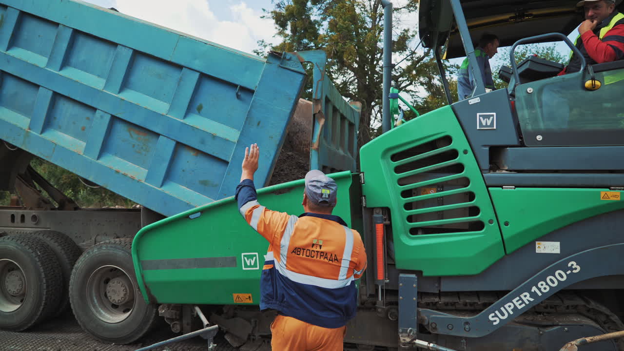 Roadworks outdoor. Truck is pouring black asphalt and a paver machine laying it on the road. Heavy machinery at street resurfacing.
