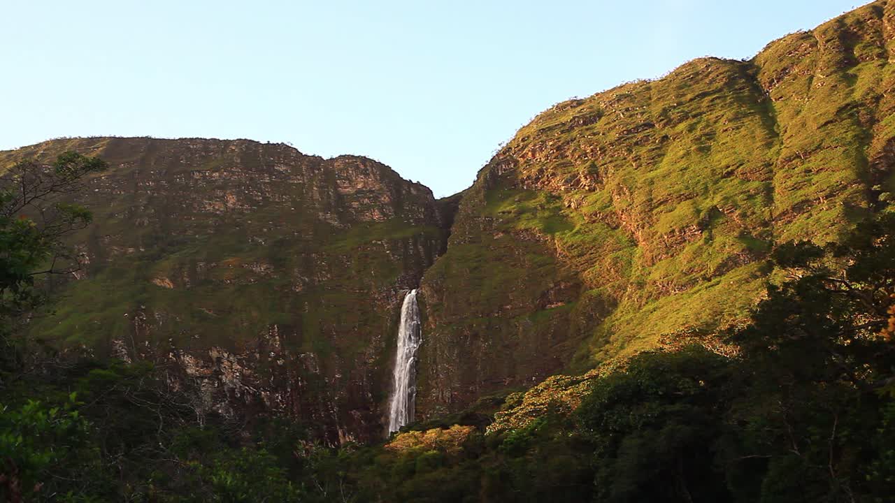 una cascada pintoresca que cae por acantilados cubiertos de plantas hacia el río y el valle de abajo