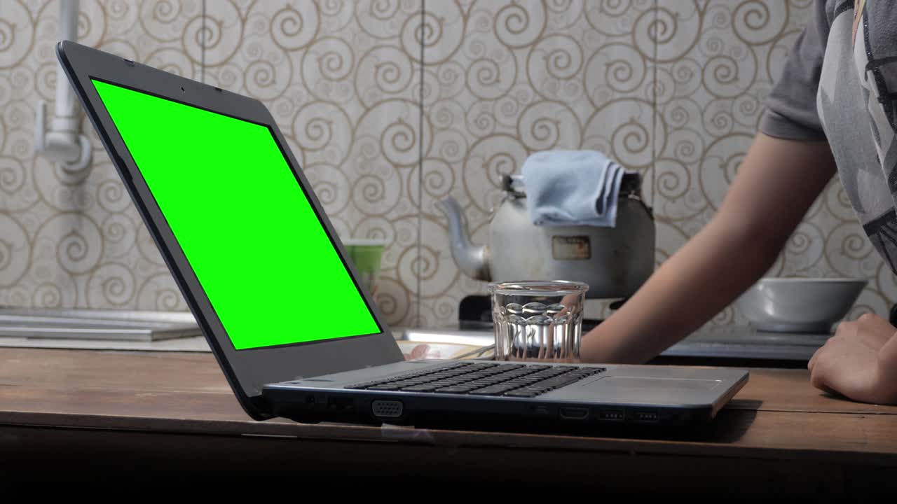 trabajar desde casa trabajando con una computadora portátil de pantalla verde en la cocina mientras hace café