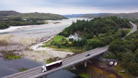 Tráfico-Conduciendo-Sobre-El-Puente-Del-Río-Morar-Cerca-De-La-Playa-De-Arena-Plateada-En-Morar,-Costa-Oeste-De-Escocia---Drone-Aéreo-4k-Hd