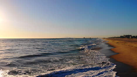 Cool,-low-aerial-drone-4k-fly-by-from-over-ocean-waves-at-sunset-to-higher,-wide-of-empty-fire-pits-at-Huntington-Beach-in-beautiful-Southern-California