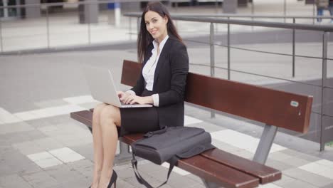 Frau-Schaut-Mit-Laptop-Auf-Bank-Herüber