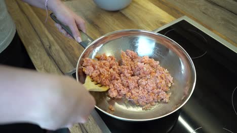 woman stirring minced meat in a frying pan with wodden spoon