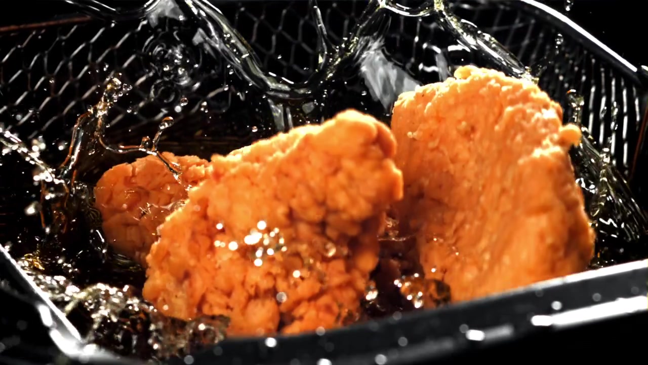 熱い油で揚げられる衣付きチキンのスローモーション