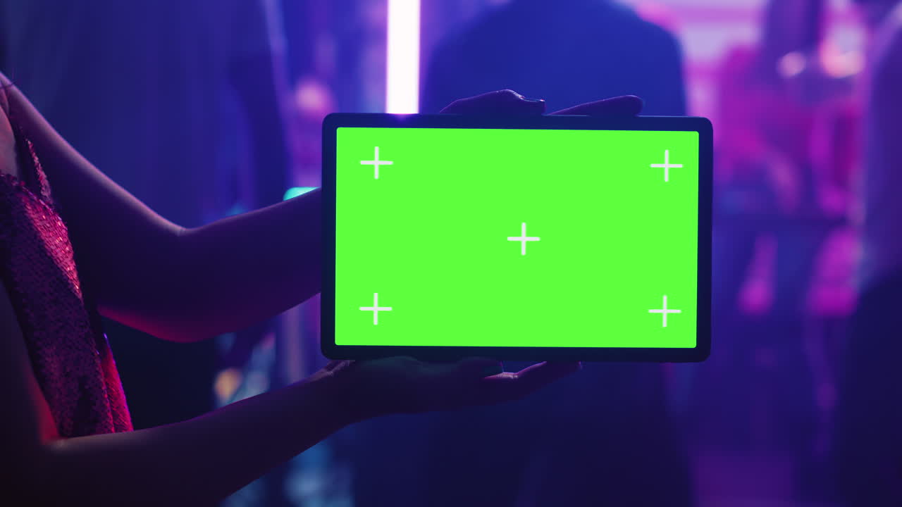 Persona che tiene in mano un tablet con schermo verde in un locale notturno