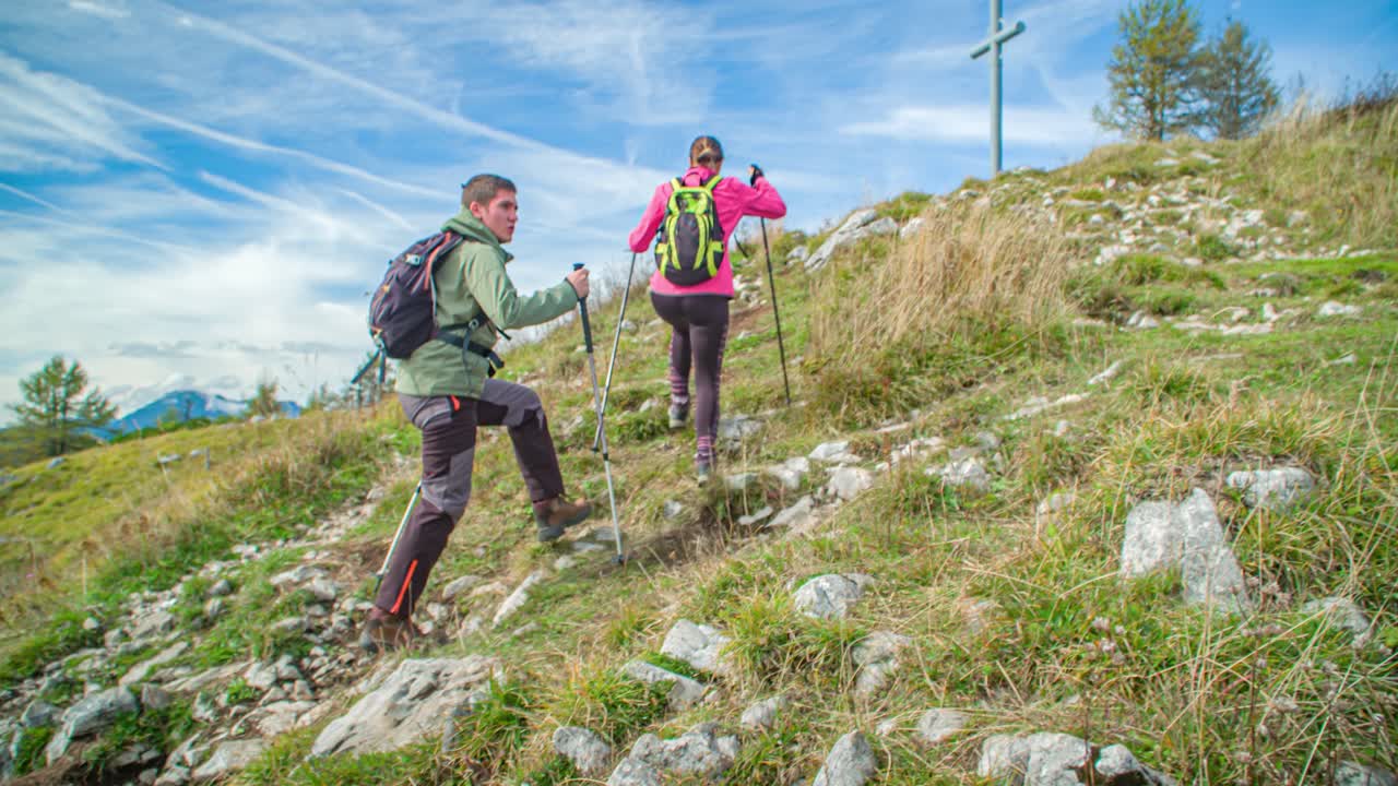 Young Hiking Couple Climbing Hill Using Trekking Poles. Follow Shot, Slow Motion