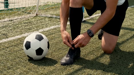 primer plano de un jugador de fútbol irreconocible atando sus zapatos de fútbol en un campo de fútbol callejero