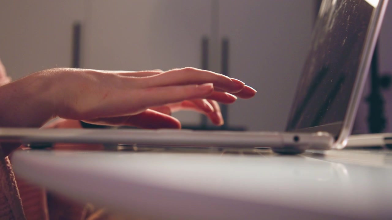 Low-angle tight crop showing hands and wrists typing on laptop placed on light desk, fingers extended and blurred between keystrokes to convey continuous rapid motion and focused work