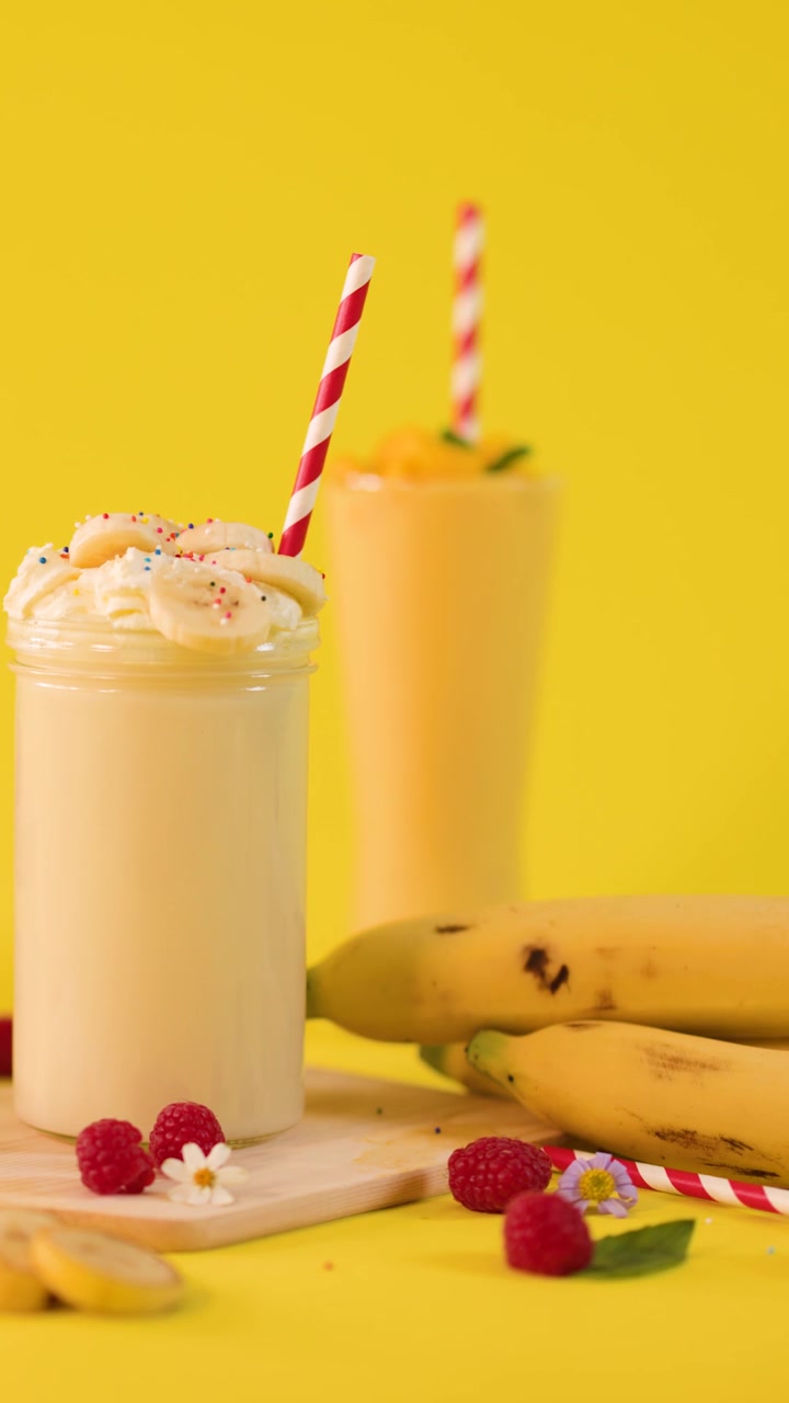 La mano di una persona inserisce una cannuccia a strisce rosse e bianche in un cremoso milkshake alla banana.