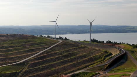 Giro-Aéreo-Revela-Terrazas-De-Vertedero-En-La-Ladera,-En-Lo-Alto-Del-Río-Susquehanna,-Turbinas-Eólicas-Girando-El-Día-De-Verano