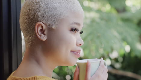 Happy-biracial-woman-drinking-coffee-at-window-at-home-in-slow-motion