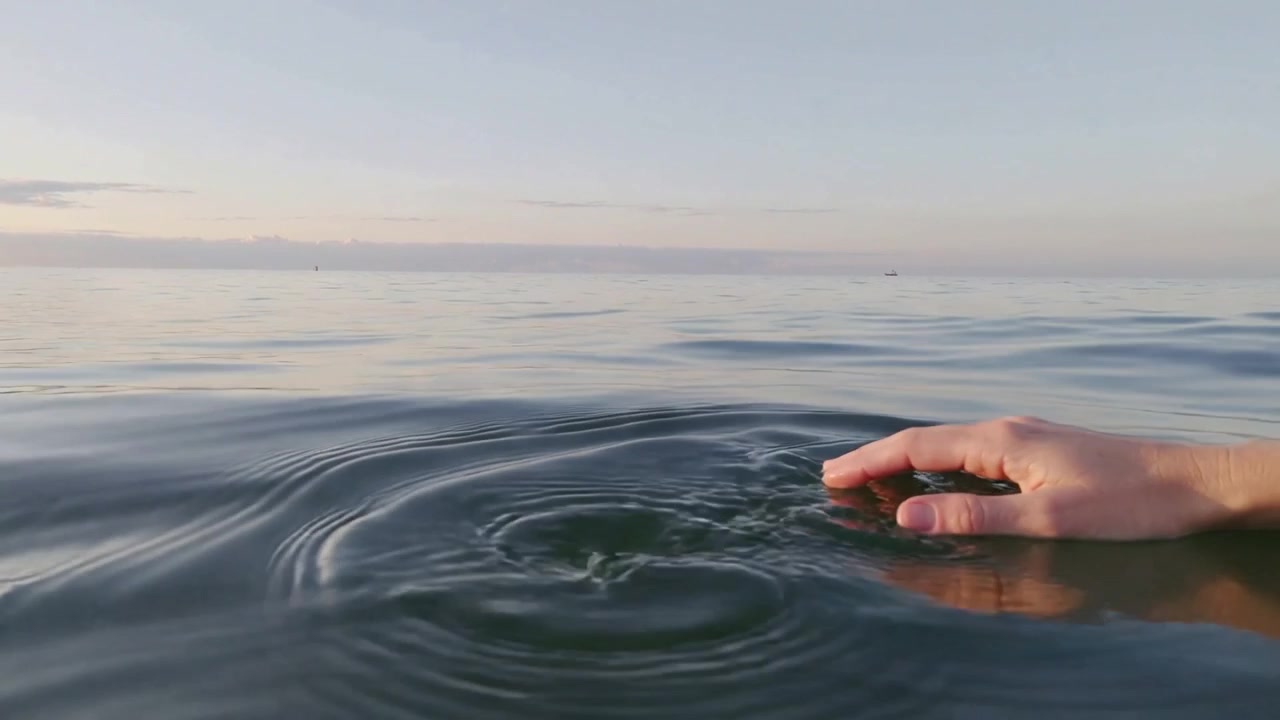 Mano destra che si abbassa creando increspature concentriche sul mare aperto vicino all'orizzonte, anello visibile, spazio per il testo.