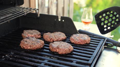 hamburger patties sizzling on grill with glencairn glass of whisky bourbon whiskey near water