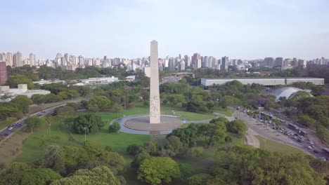 Traffic-around-Ibirapuera-park-and-Obelisco-monument-in-Sao-Paolo,-Brazil--ascending-aerial-drone-shot