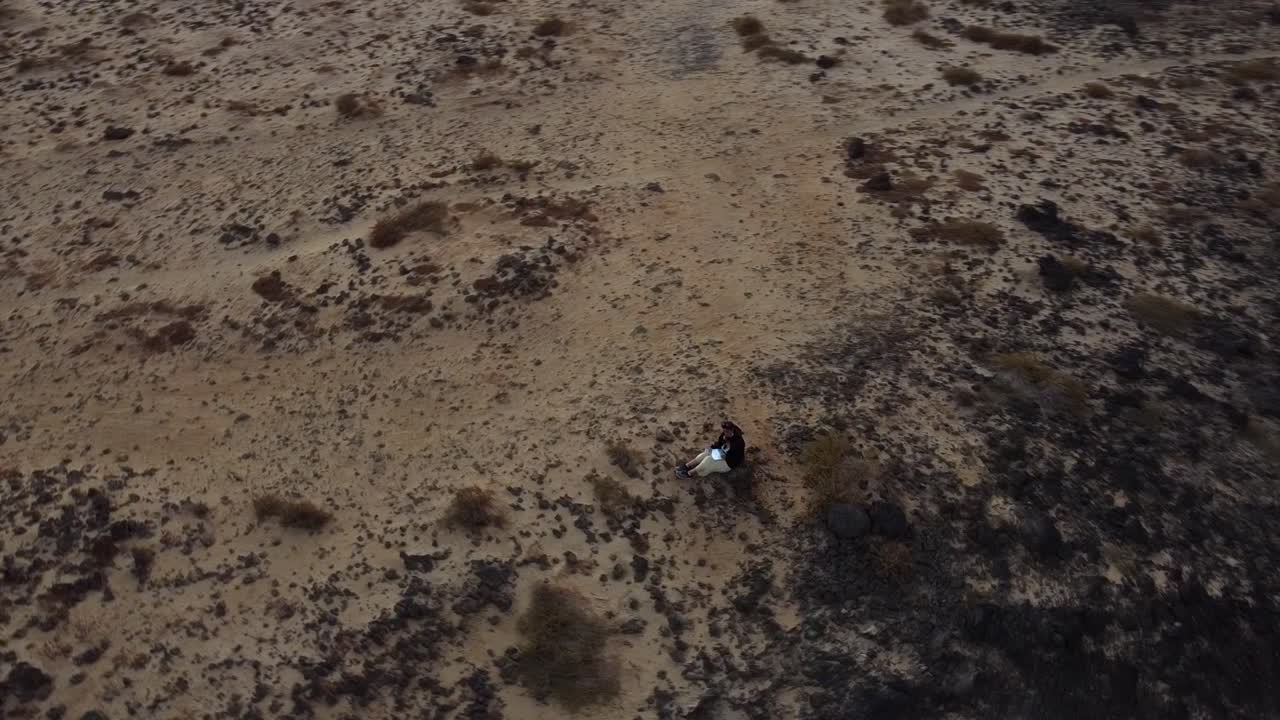 Woman Sitting On Sandy Coast While Reading In Punta de la Pared In Lanzarote, Spain. aerial drone orbit