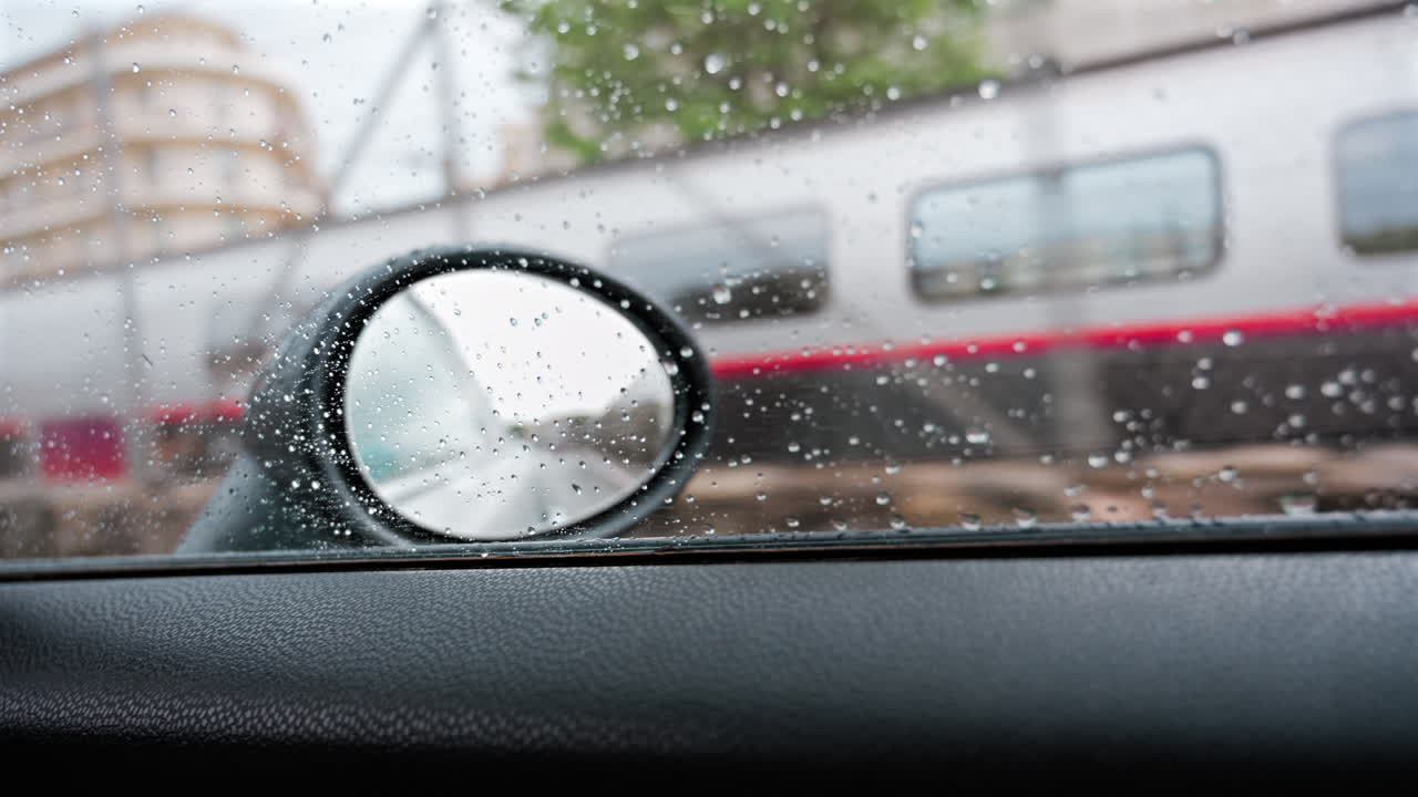 Close up of raindrops on a car window with the a view of the mirror and a train passing by
