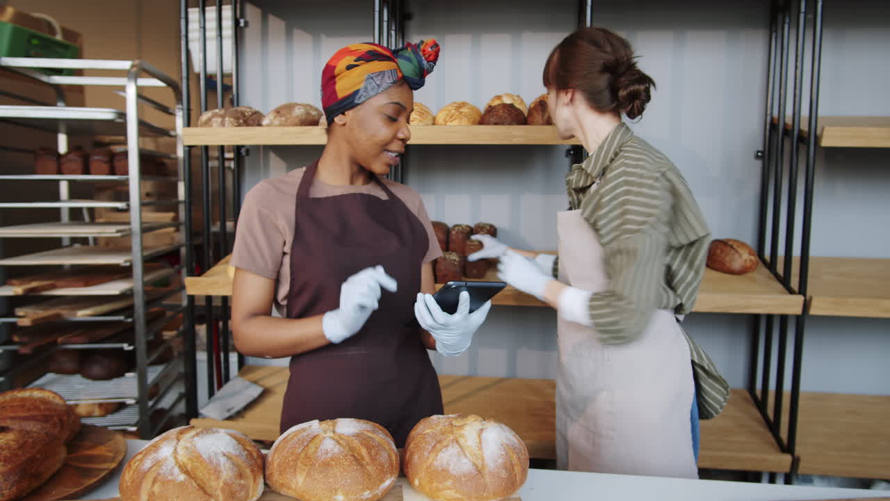 dos colegas femeninas diversas usando una tableta mientras trabajan en una panadería