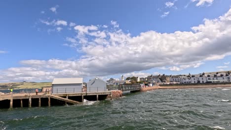 wide shot of cromarty waterfront with pier, choppy sea, and bright daylight. camera pans smoothly, capturing coastal town architecture and dynamic sky