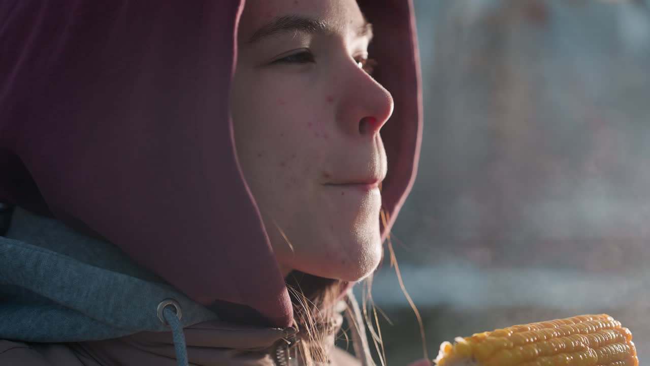 primer plano de una mujer joven comiendo maíz con vapor caliente proveniente del maíz, sintiendo calor en el clima frío, bocadillo de maíz fresco al aire libre en invierno, persona disfrutando de la comida