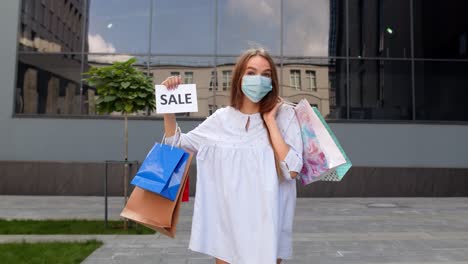 girl in protective mask with shopping bags showing sale word inscription during coronavirus pandemic