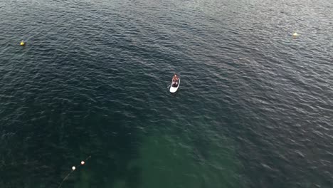 man kneeled on stand up paddle paddling close to yacht, aerial orbiting overhead view