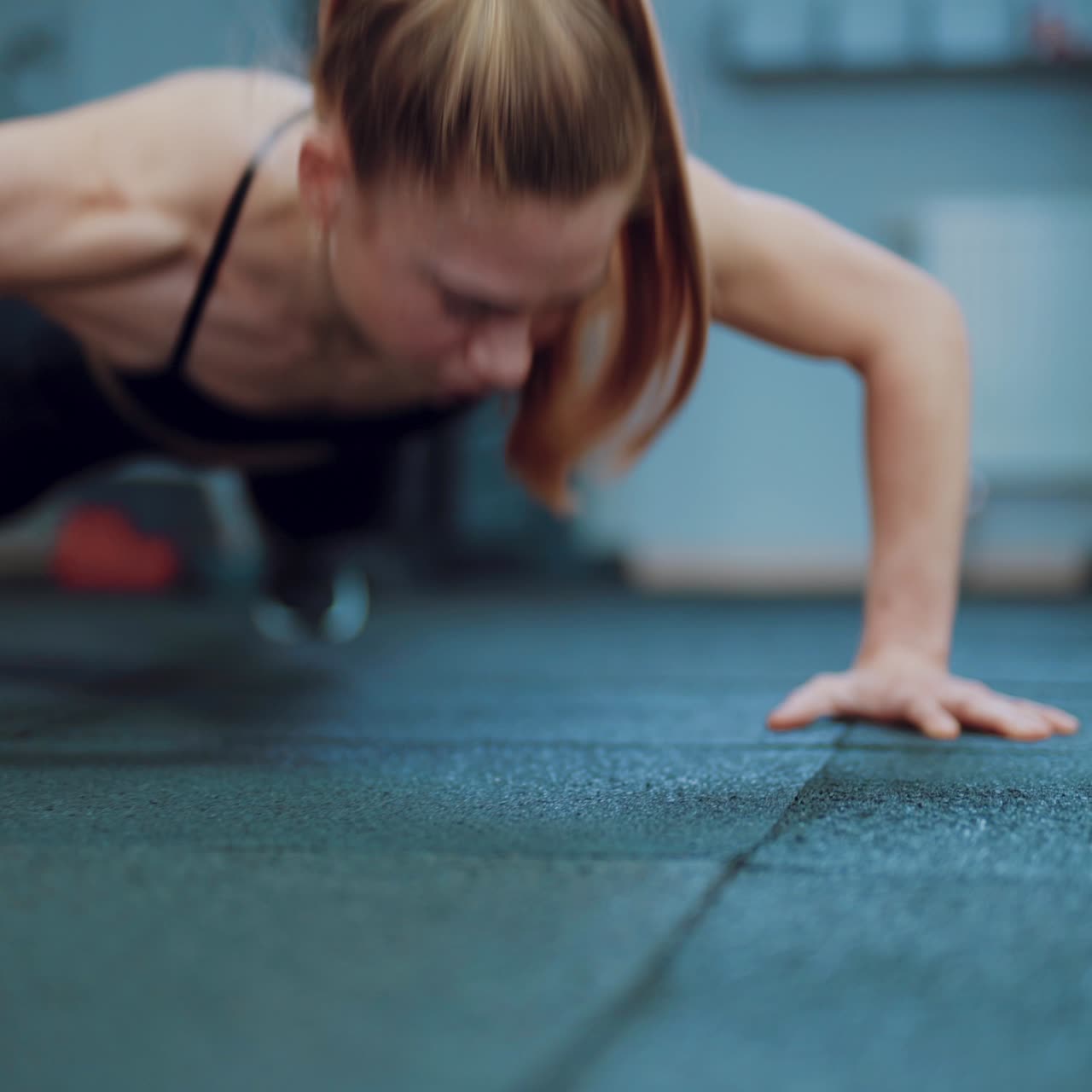 A strong woman with a ponytail push up from the floor in the gym. Blurred background. Camera motion forward