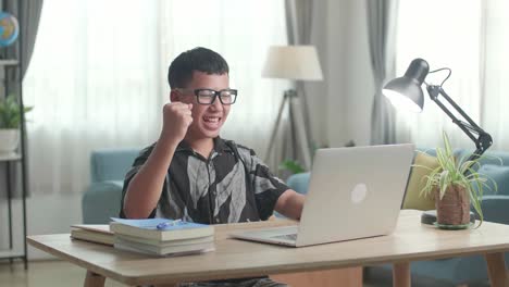 young asia boy student celebrating with laptop at home, teenage boy learning online from laptop