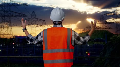 back view of a male engineer with safety helmet spreading arms while standing near high voltage tower