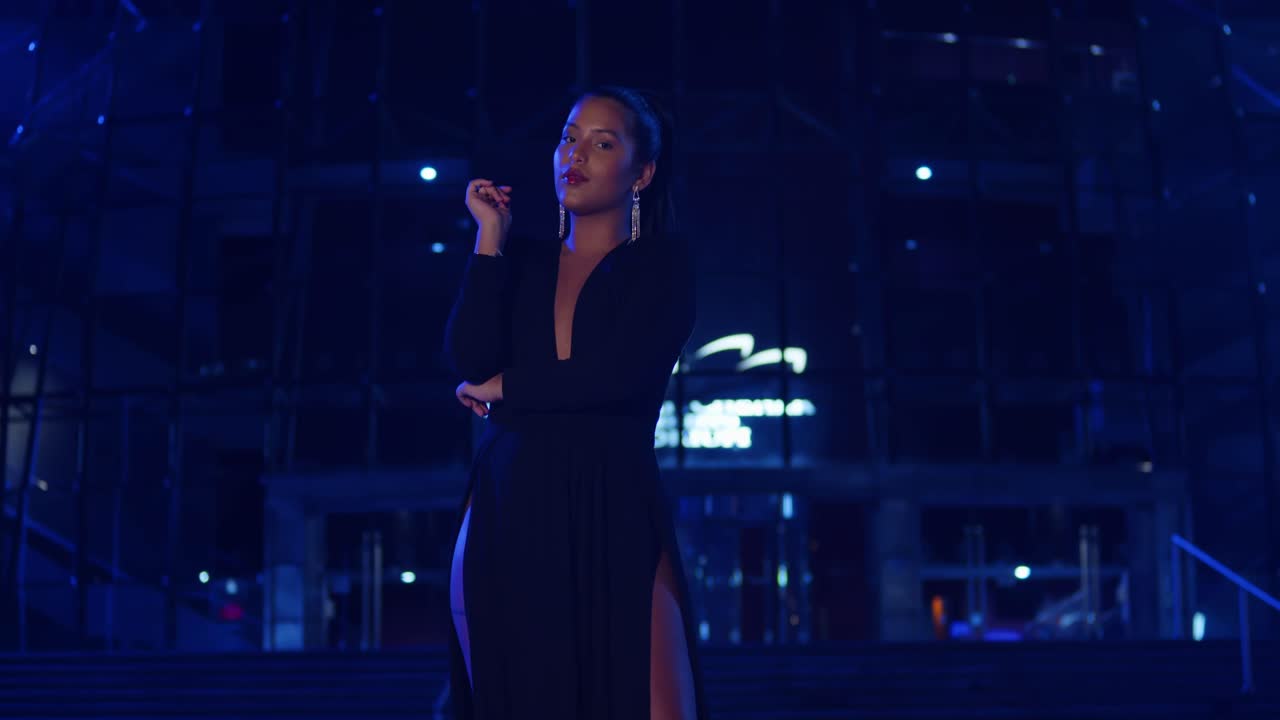 joven hispana se encuentra en la ciudad con un vestido negro con luces azules en el fondo