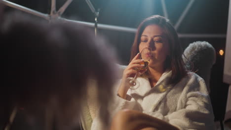 mujer tranquila levanta lentamente el vaso de alcohol a sus propios labios mirada vacía a la deriva en la distancia. señora deprimida se siente cómodo sentado en una silla suave con túnica acogedora